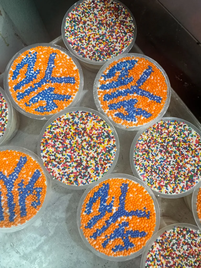 Dot cakes decorated with orange and blue sprinkles and multicolored sprinkles, in clear plastic containers.