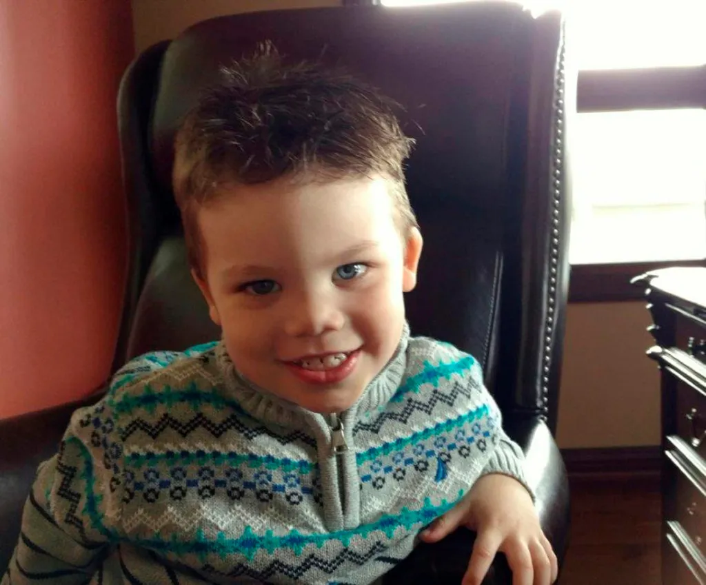 Lane Graves, a 2-year-old boy, smiling while sitting in a large armchair.