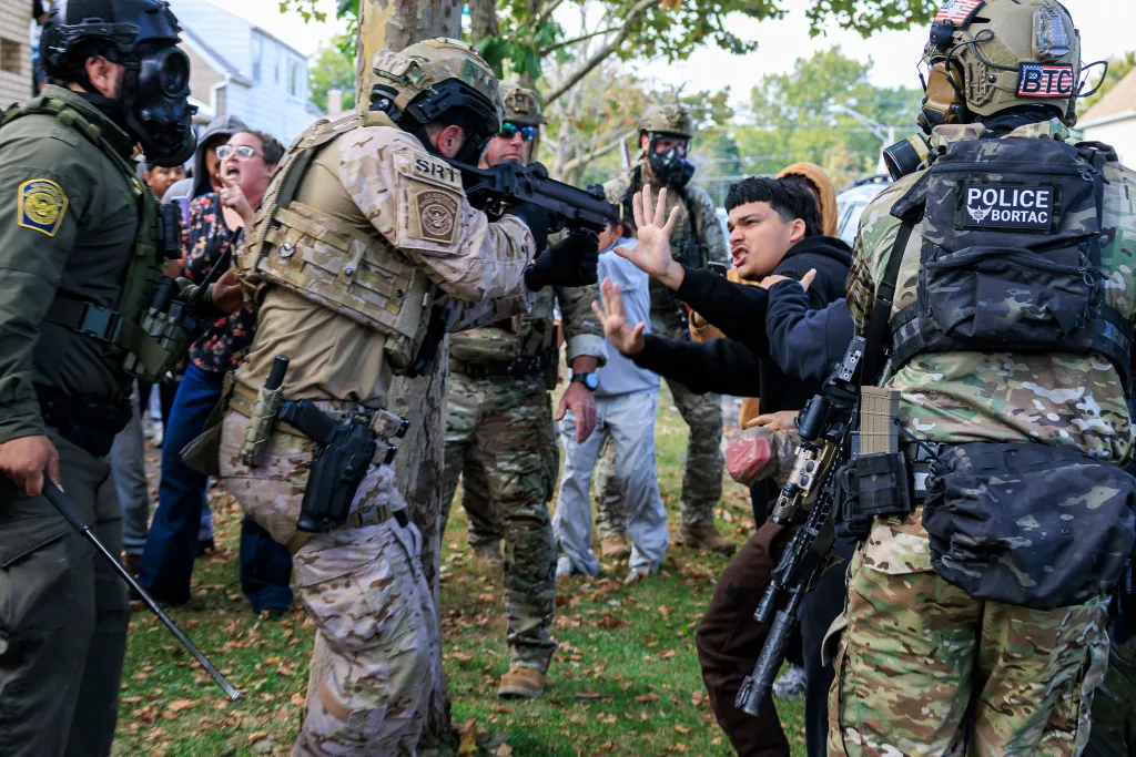 A law enforcement officer points a crowd control weapon at a protester in East Side, Chicago.