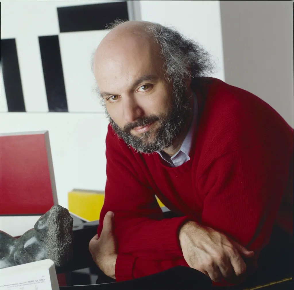 Portrait of James Burrows, a bald man with a beard and gray hair, wearing a red sweater.