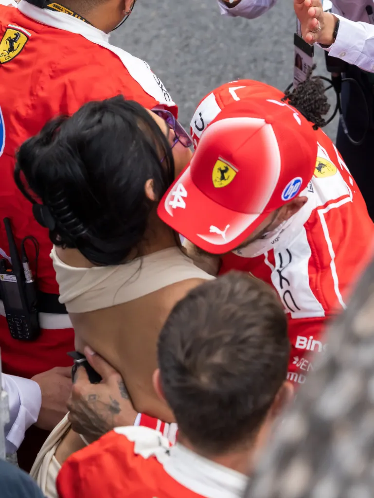 Lewis Hamilton in a red Ferrari racing suit and hat, and Kim Kardashian in a beige top, embrace at the F1 Grand Prix of Monaco.