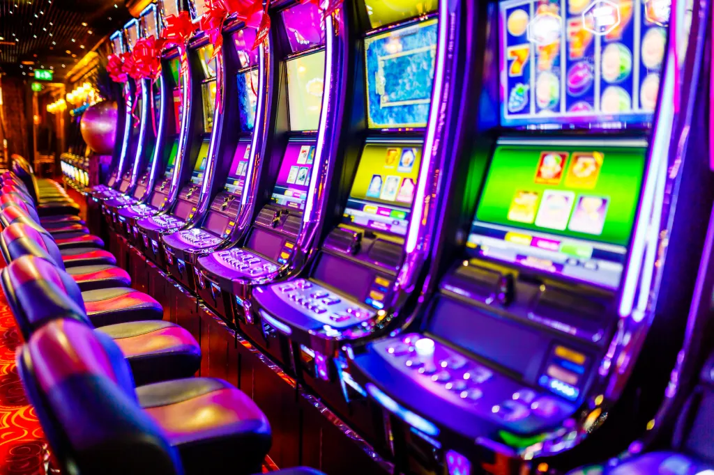 Line of electronic slot machines in a casino with chairs in front of each machine.