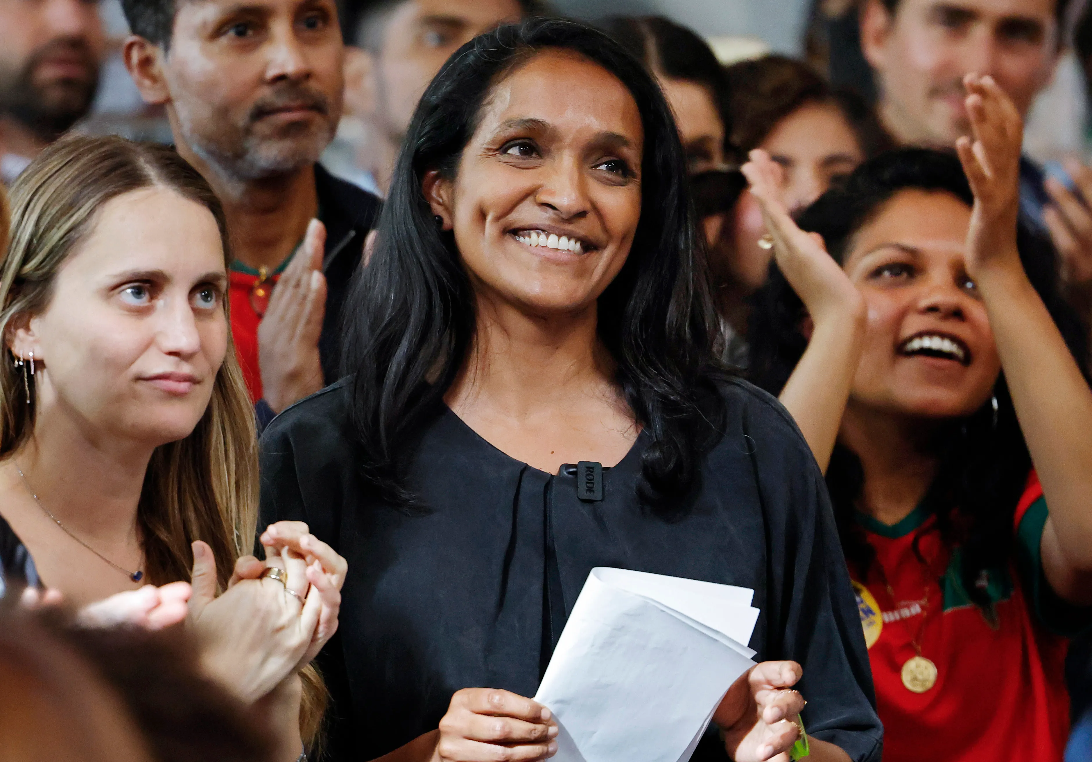 Los Angeles Mayoral Candidate Nithya Raman smiles, holding papers, with supporters cheering and clapping around her.