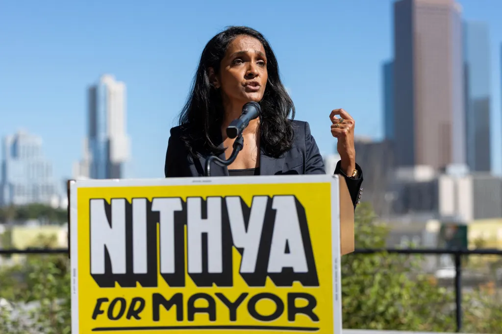 Los Angeles City Councilwoman Nithya Raman speaking at a podium with a campaign sign reading 