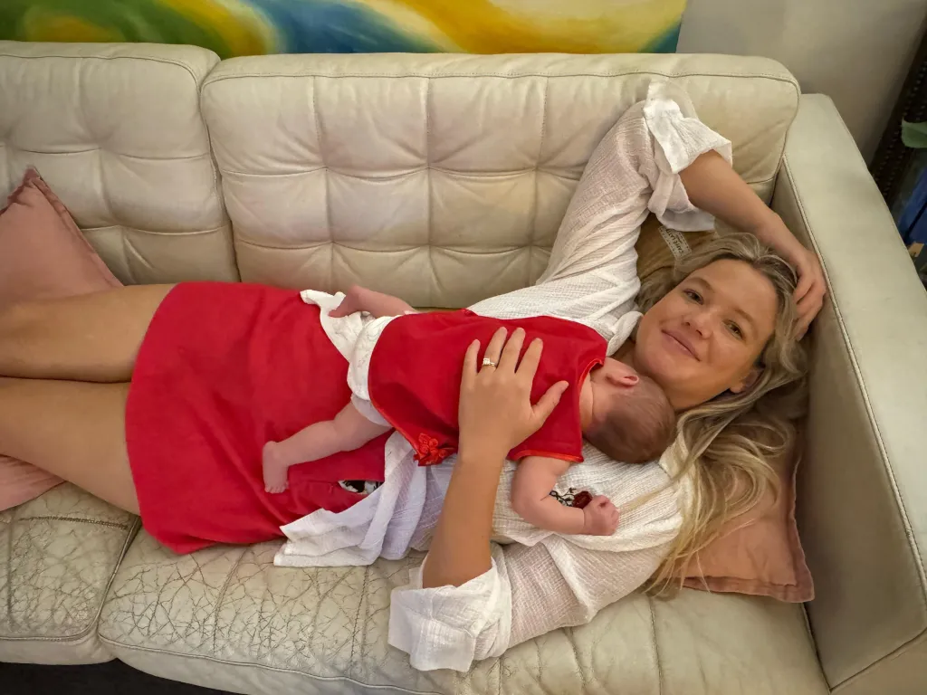 Leah Stewart, a blonde woman, lying on a couch with a baby asleep on her chest.