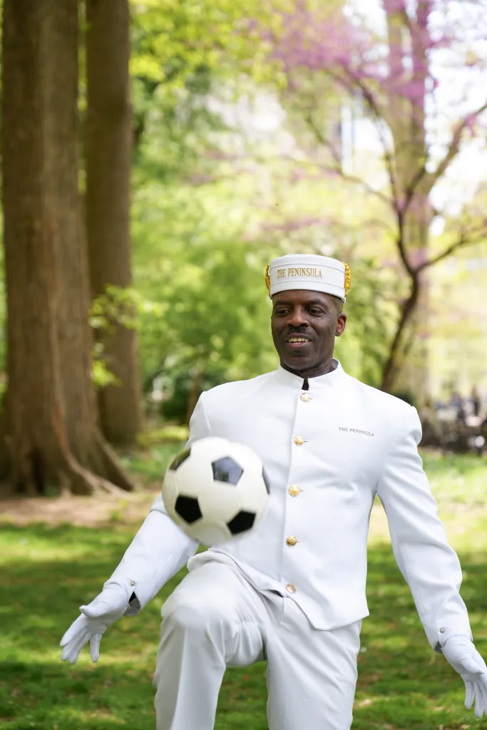 A man in a white Peninsula uniform juggling a soccer ball on his knee.