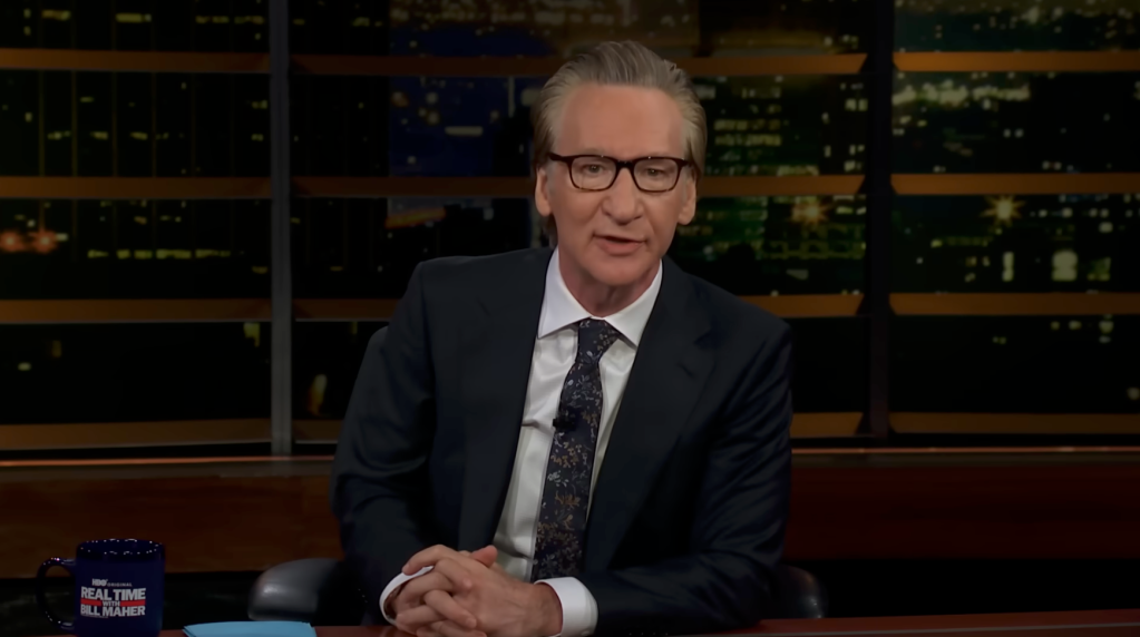 Bill Maher sits on a set of 