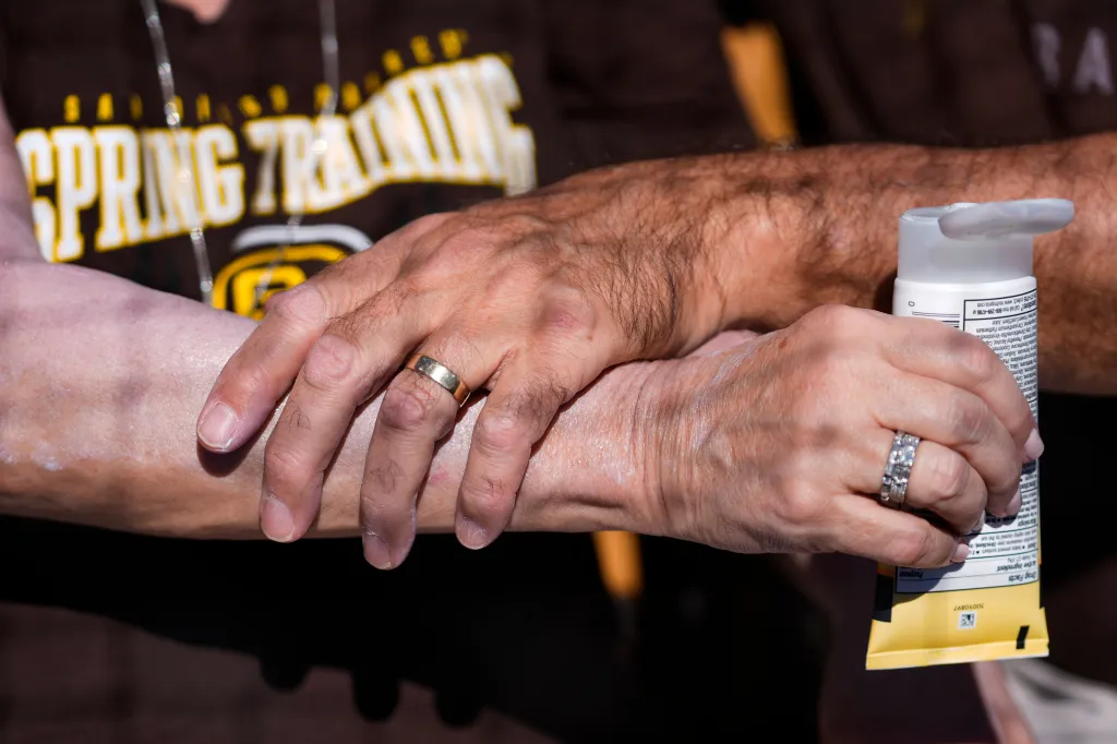 A man applies sunscreen to a woman's arm before a spring training baseball game.