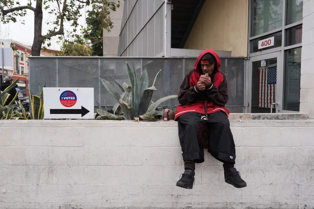 A man in a red hoodie lighting a cigarette outside a voting center with an 
