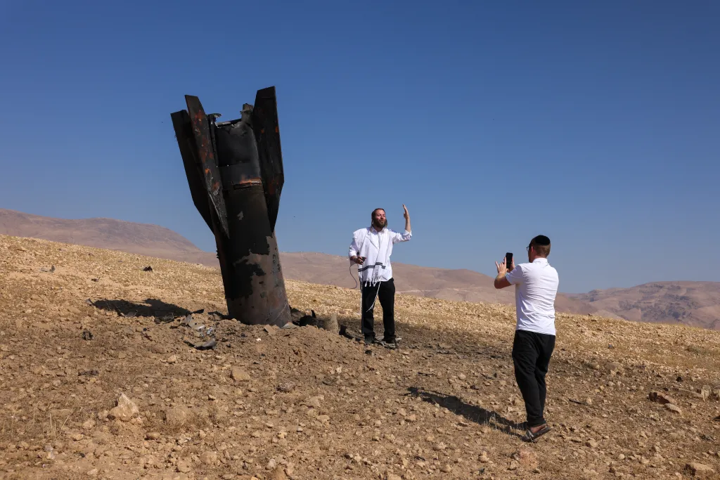A man in a tallit poses for a photo next to a fallen rocket in Jericho.