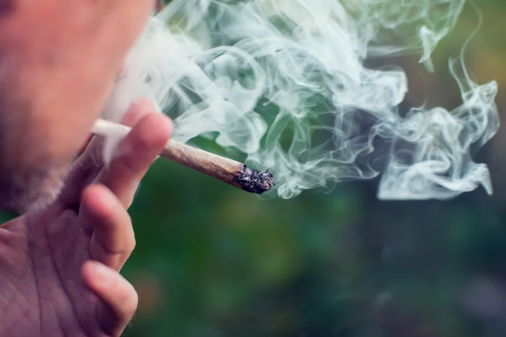 A man smoking a joint, exhaling a plume of smoke.