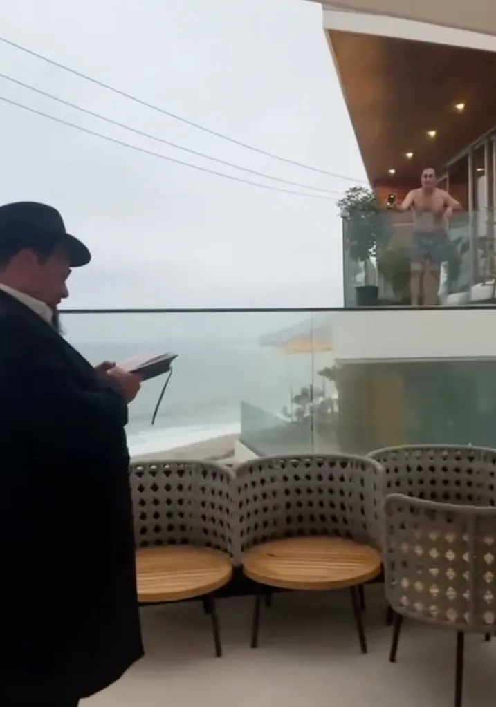 A man in a black hat reads a book on his balcony while another man yells racial slurs from his neighboring balcony.