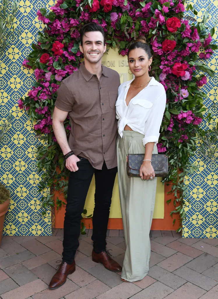 Mason Trueblood and Justene Alpert pose together in front of a floral backdrop.