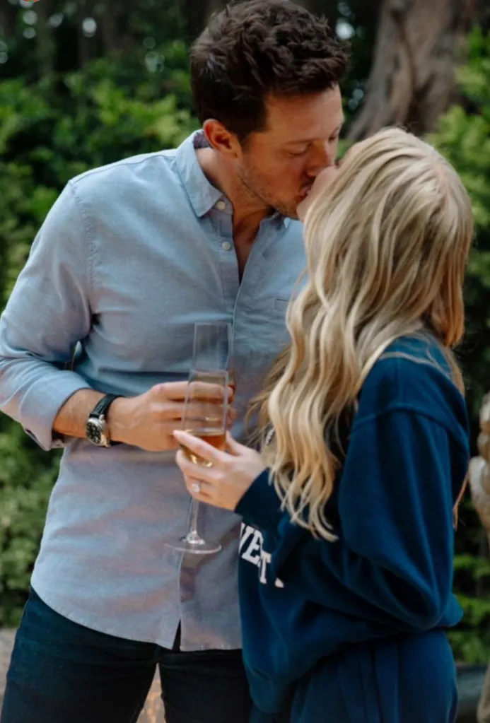 Matt Kaplan and Alex Cooper kissing, holding champagne flutes.
