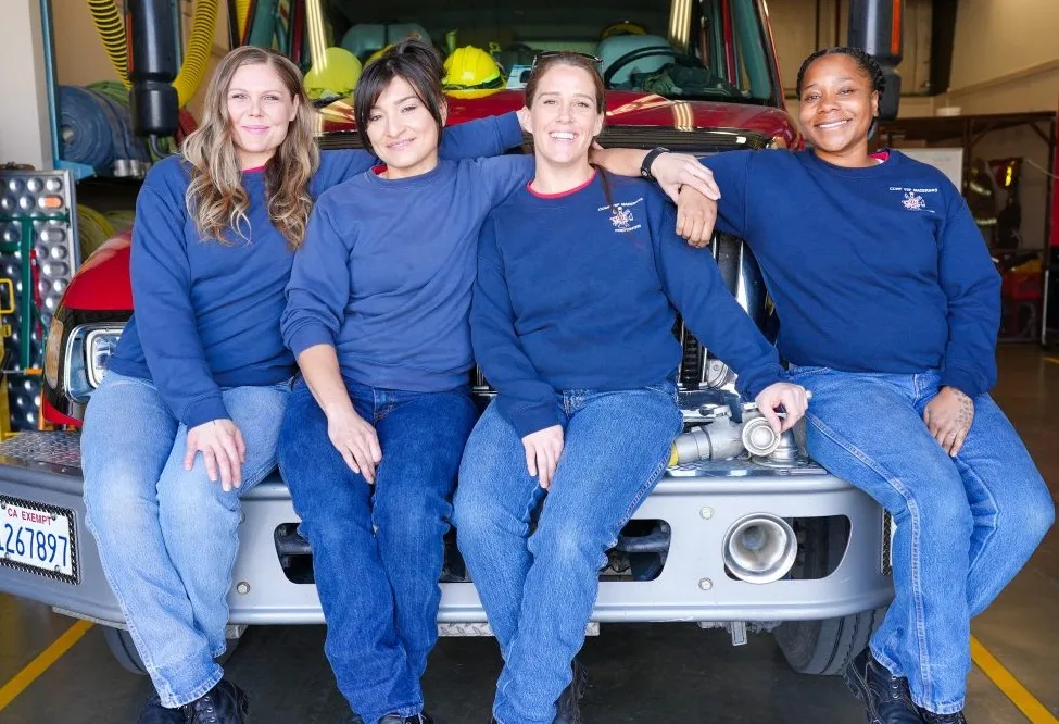 Four women firefighters sitting on the front of a fire truck.
