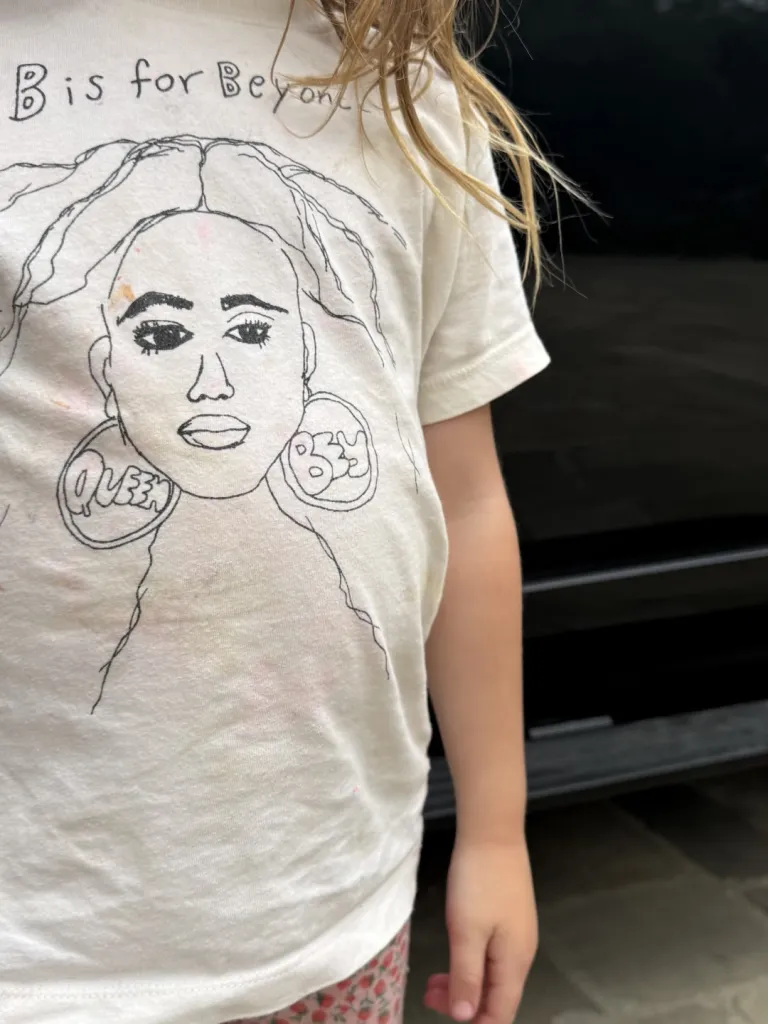 A child wearing a white t-shirt with a drawing of Beyoncé, featuring large hoop earrings that say 