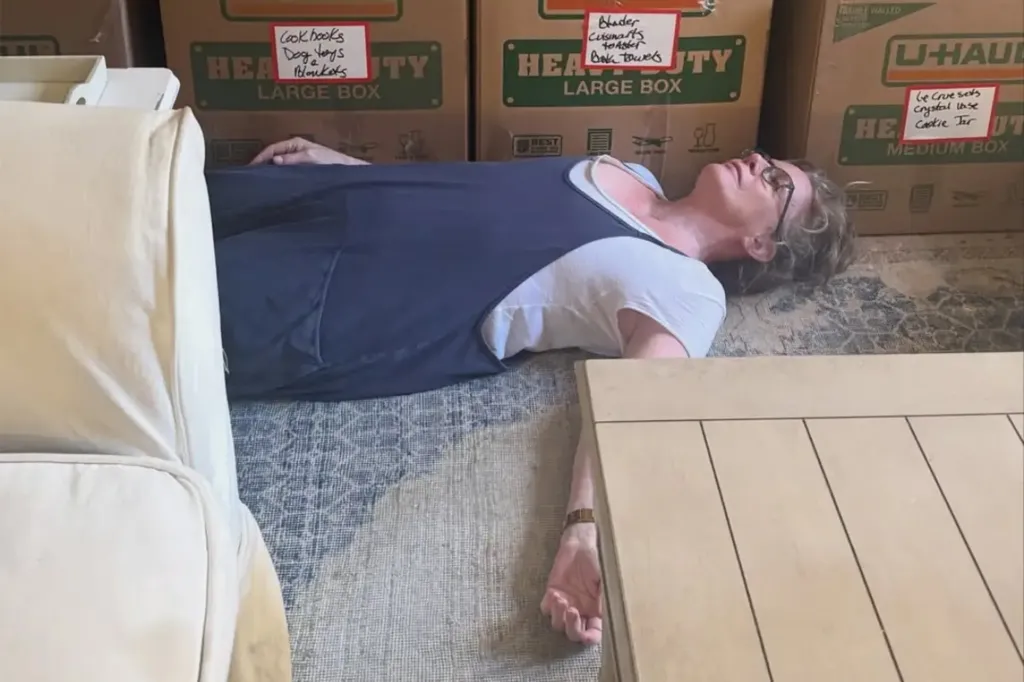 A woman lying on the floor surrounded by moving boxes.