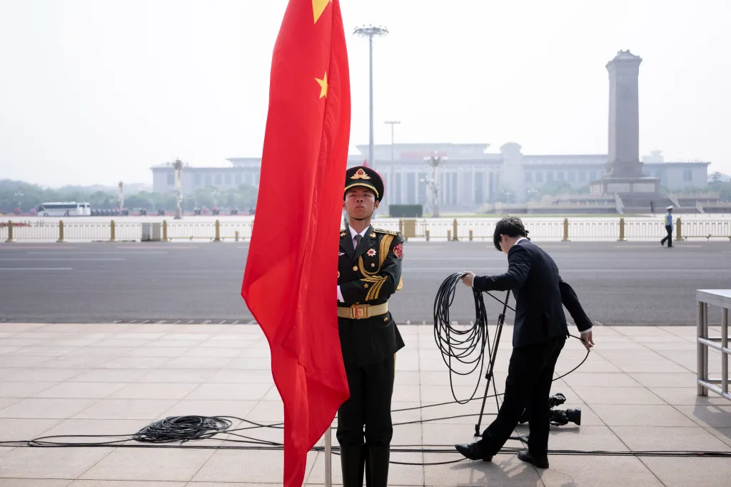 A Chinese military member stands with the Chinese flag as a staff member prepares for a welcome ceremony in Beijing.