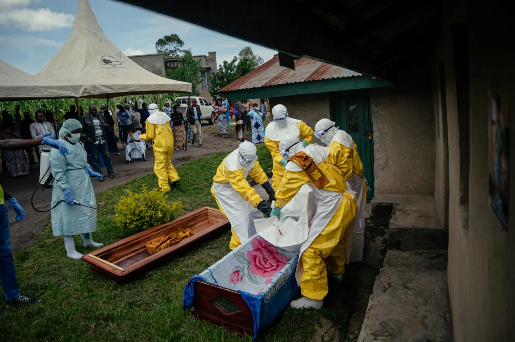 Congolese Red Cross team in PPE placing the body of a woman suspected of dying from Ebola into a coffin.