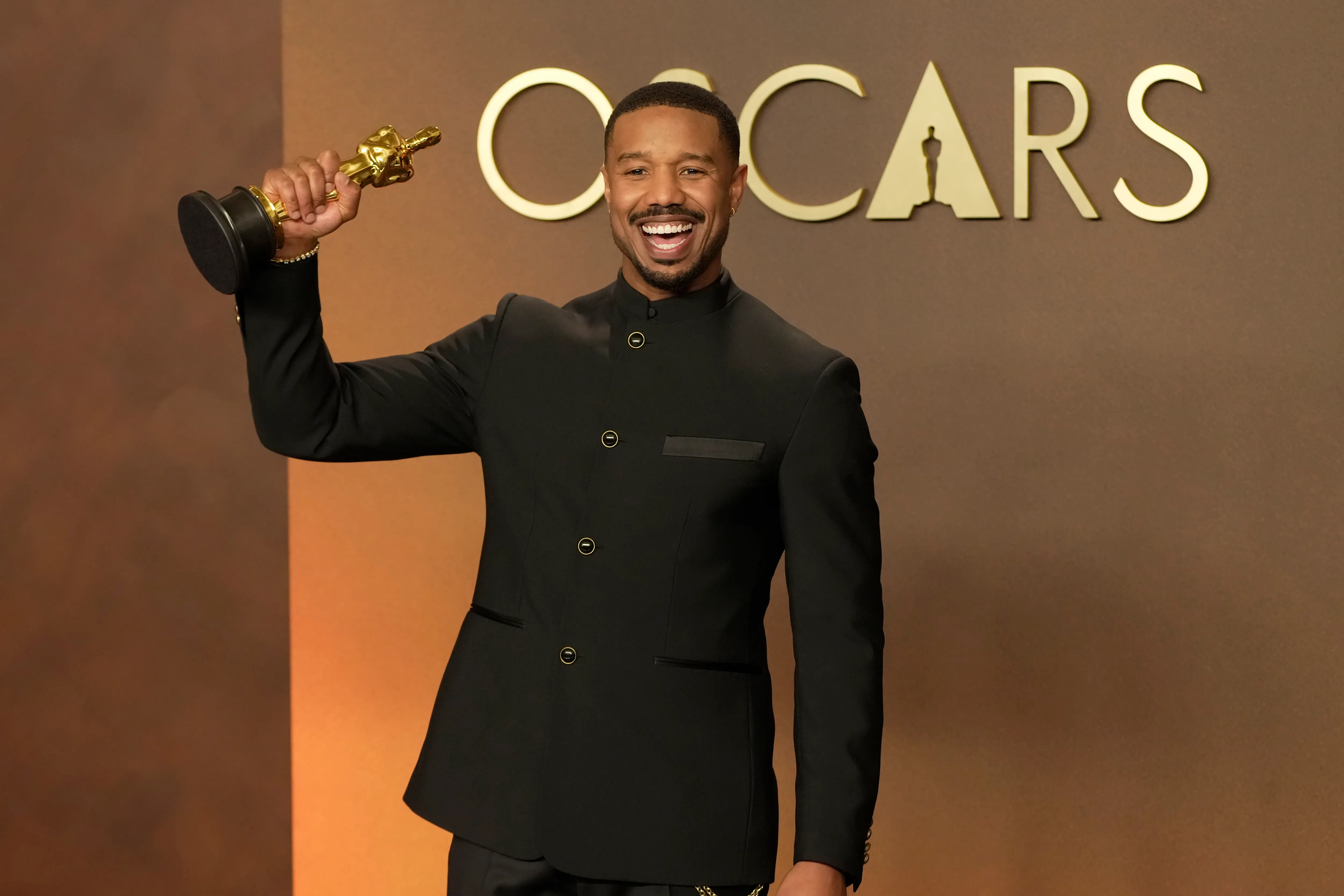 Michael B. Jordan smiles, holding his Best Actor Oscar aloft.