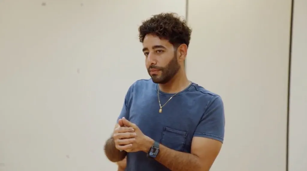 Mido standing with his hands clasped together during an argument.