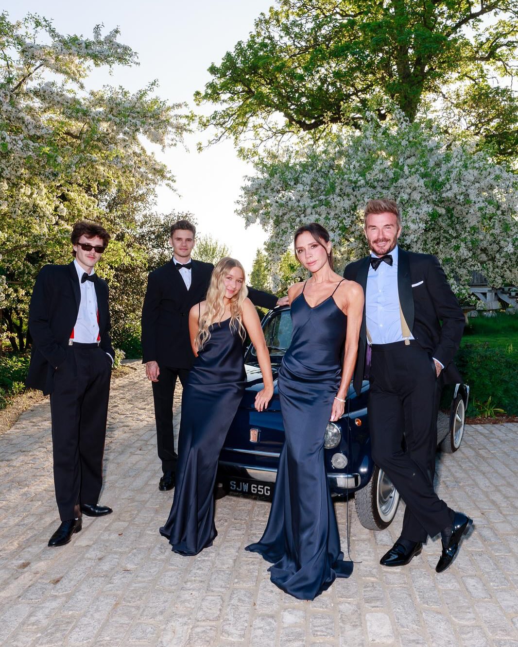 The Beckham family (minus Brooklyn) posing in formal wear beside a vintage blue car.