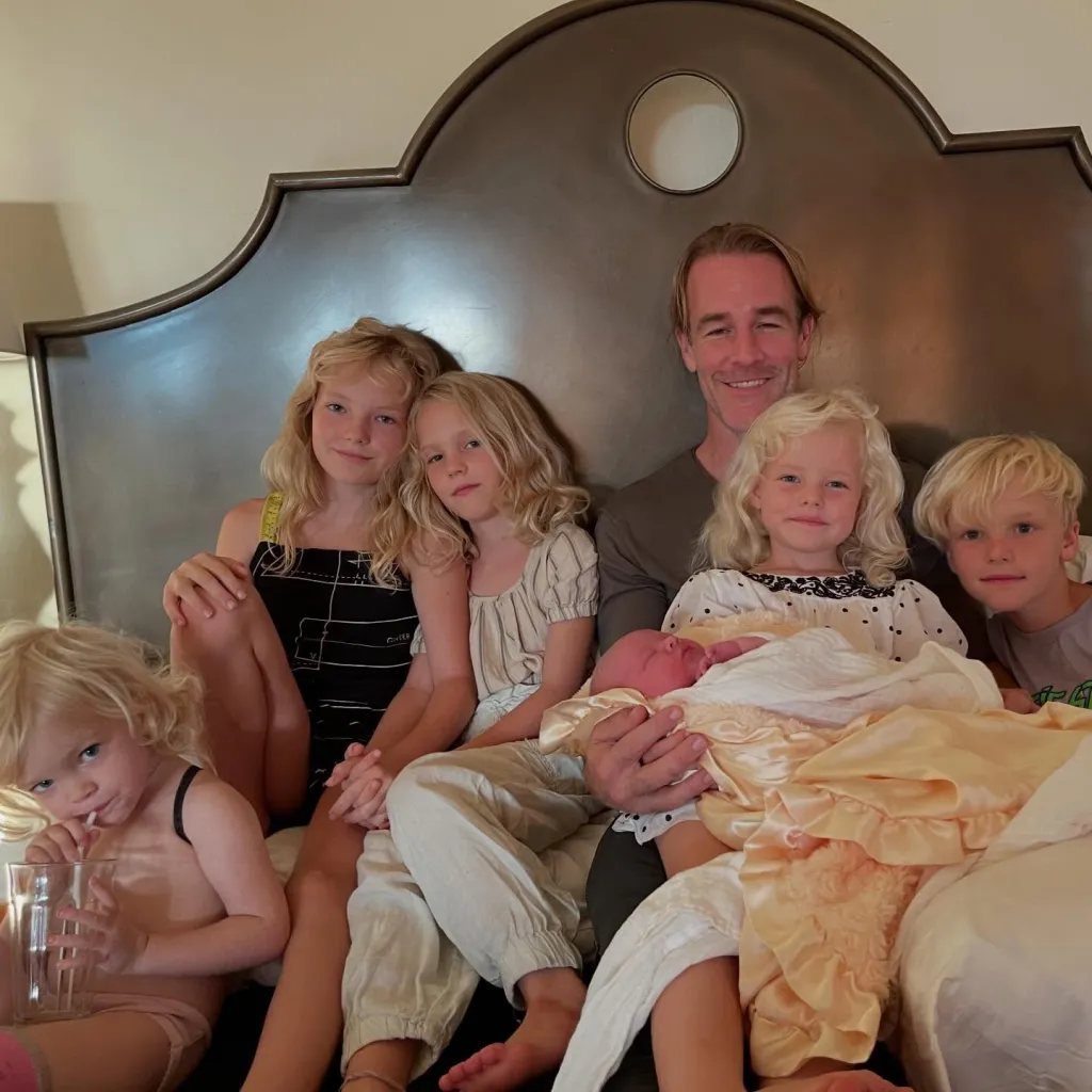 James Van Der Beek sitting on a bed with his five children, including a newborn wrapped in a peach blanket.