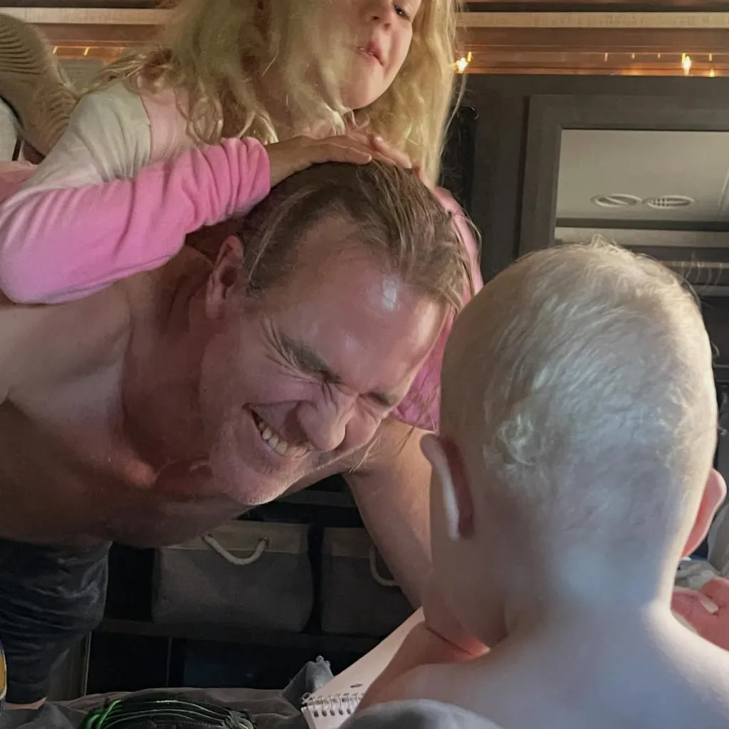 James Van Der Beek with his two children, one on his back and one in front of him, all smiling.
