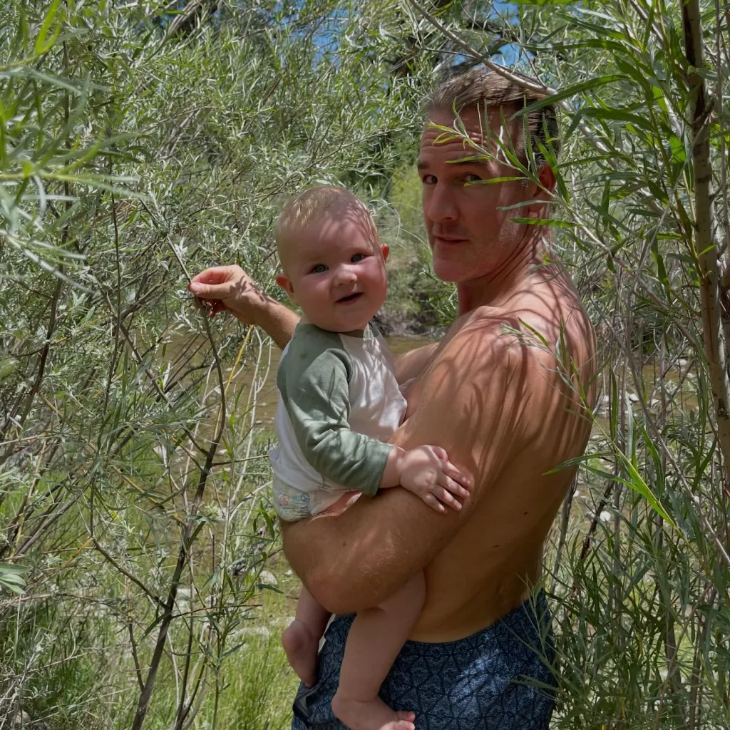 James Van Der Beek holding a baby next to a stream.