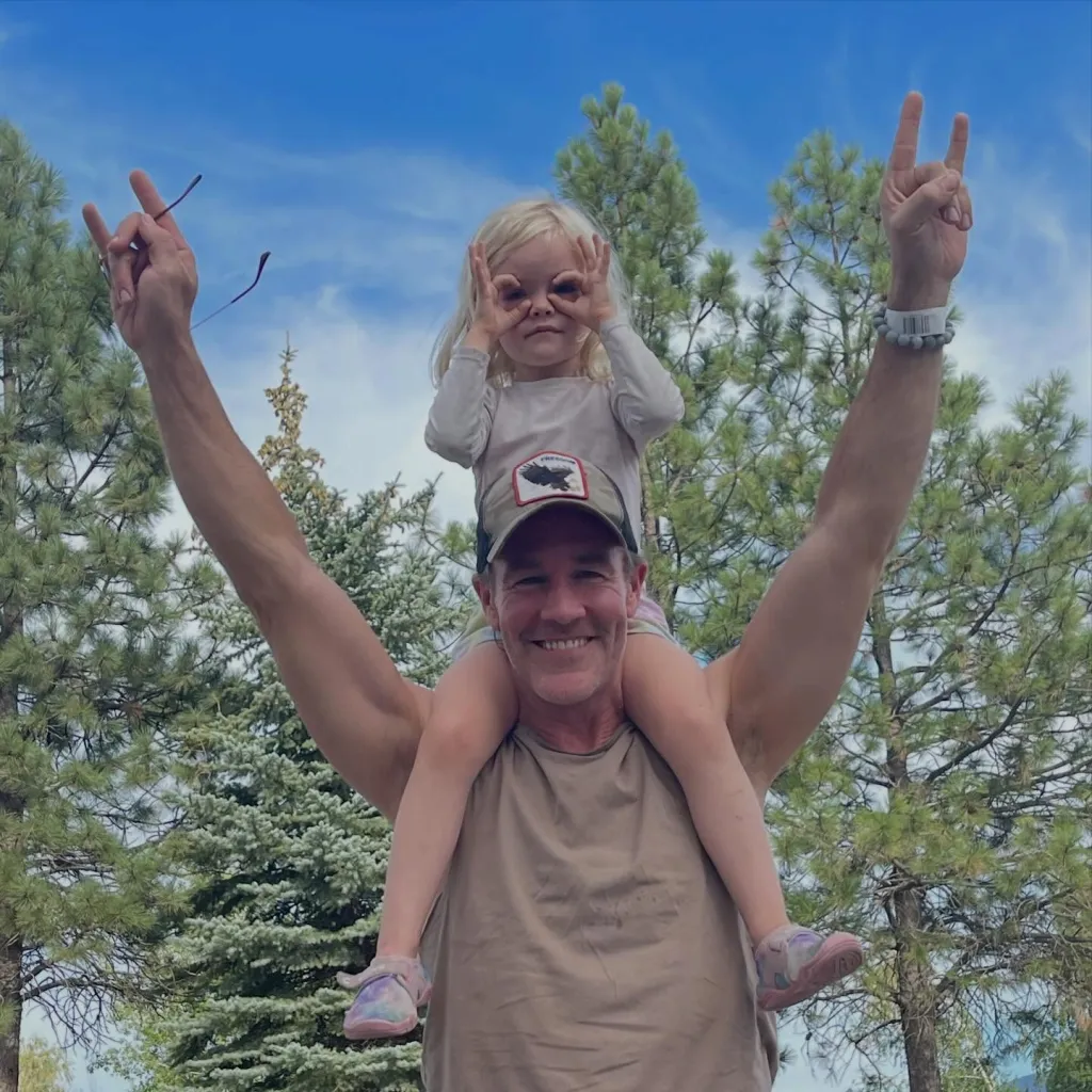 James Van Der Beek giving his daughter a piggyback ride, both making funny hand gestures.