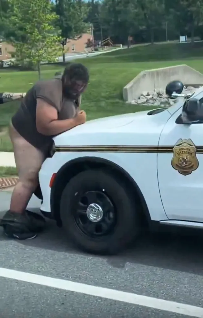 A man with his pants around his ankles leaning on the hood of a police car.