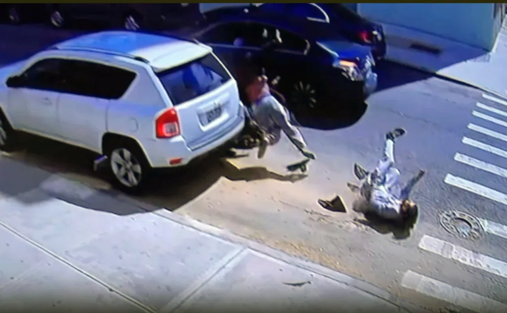 Two people lying on the ground next to a white SUV after being thrown from a moped in a collision.