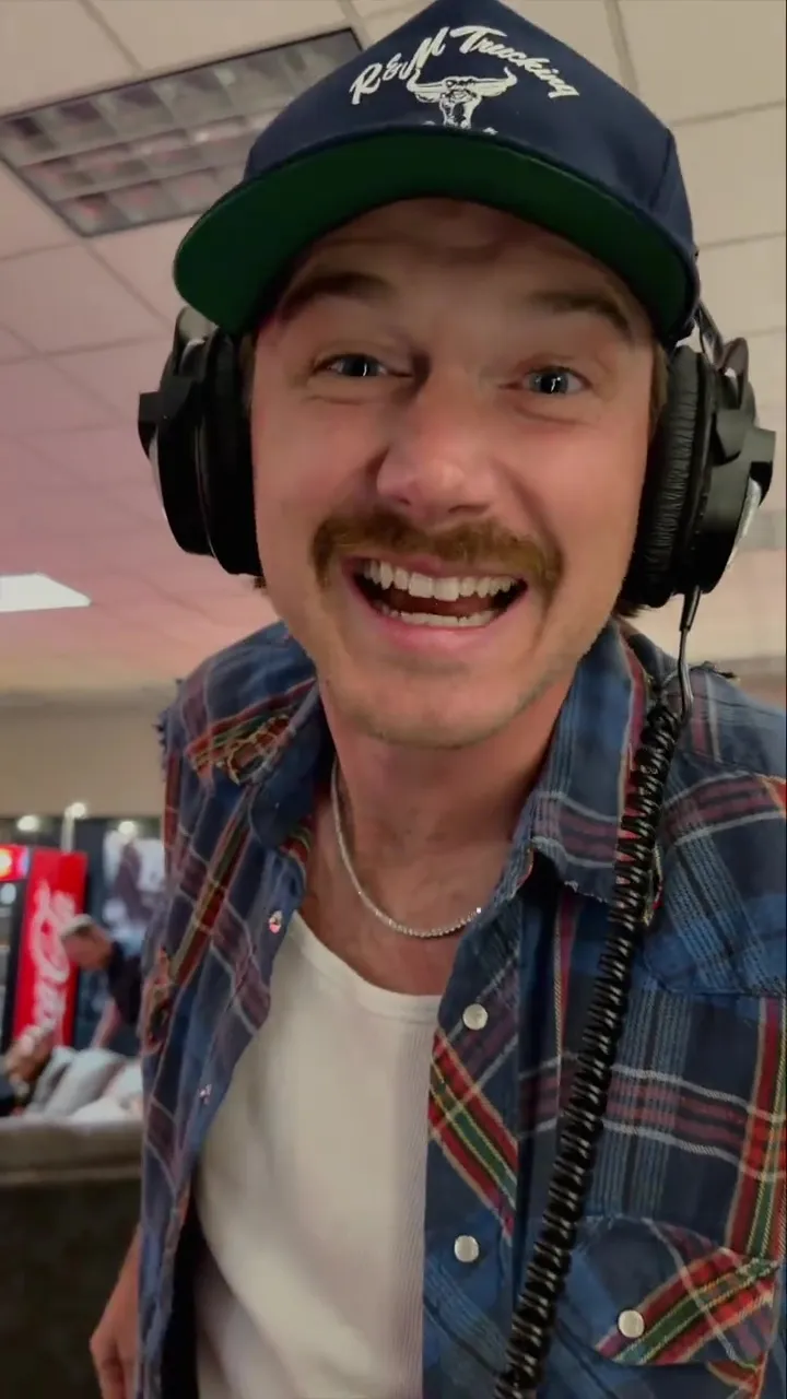 Morgan Wallen laughing while wearing headphones and a cap.