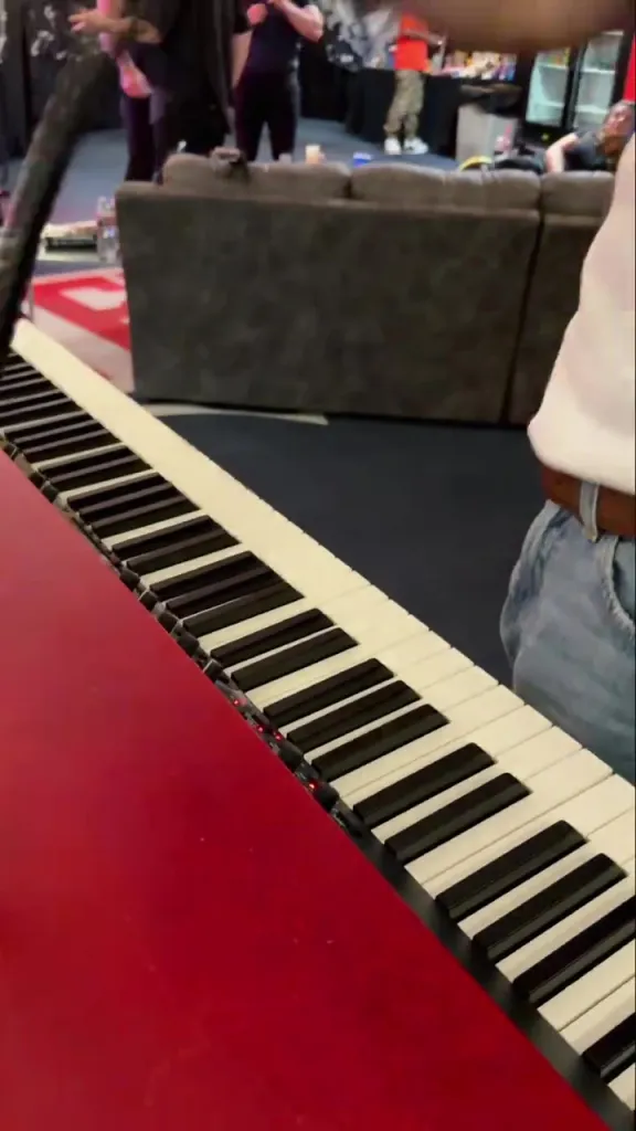 A red piano with black and white keys, as a person in a white t-shirt and blue jeans stands next to it.