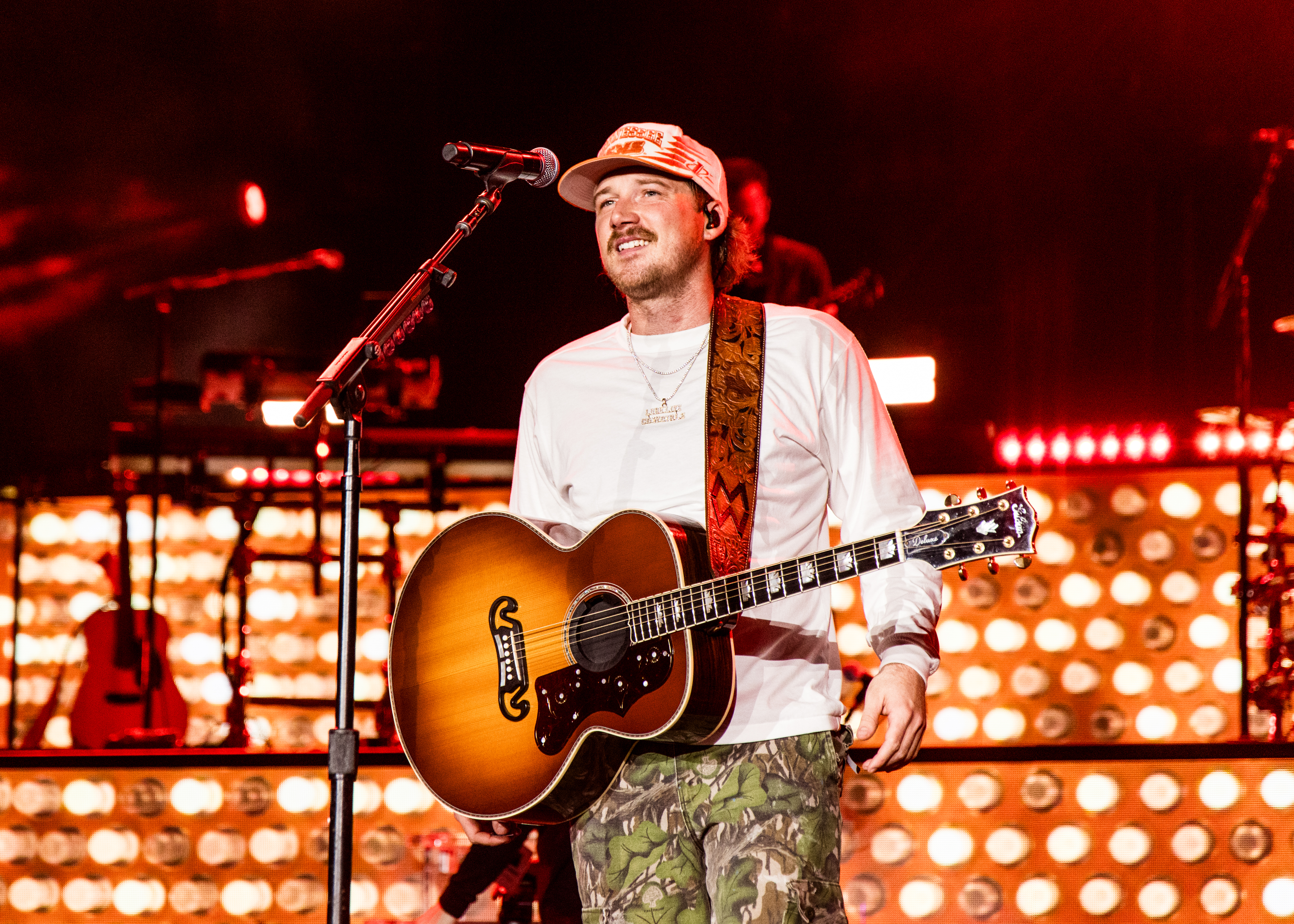 Morgan Wallen performs onstage at Neyland Stadium, holding an acoustic guitar.