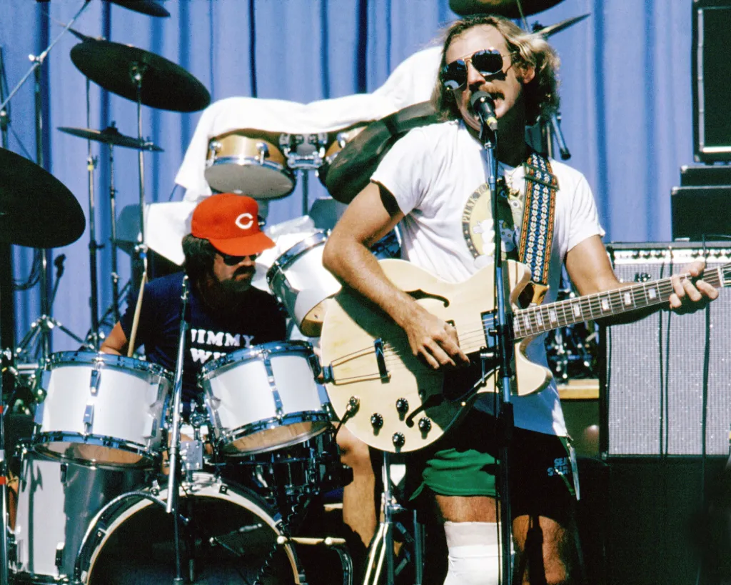 Jimmy Buffett performs on stage, playing a hollow-body electric guitar and singing into a microphone.