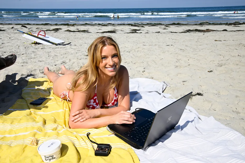 Nadia Nowak smiles while using a laptop on a beach blanket in Pacific Beach, San Diego.