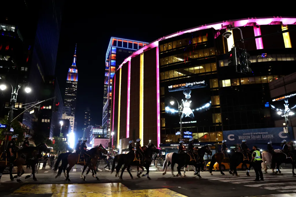 Mounted police patrol the street in front of Madison Square Garden and the Empire State Building at night.