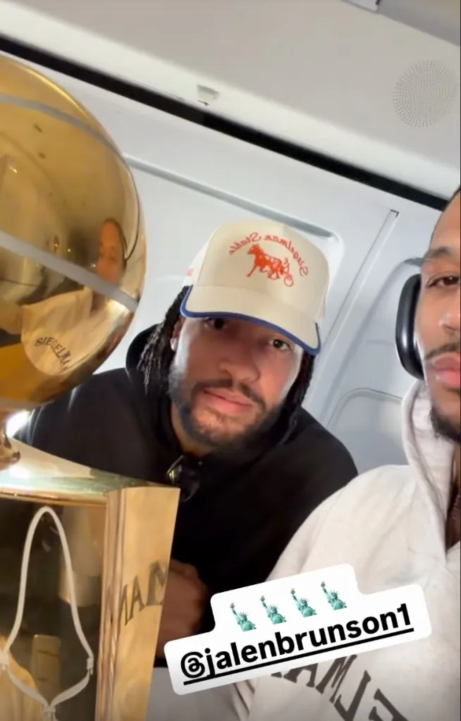 Jalen Brunson and Josh Hart with a gold trophy on an airplane.