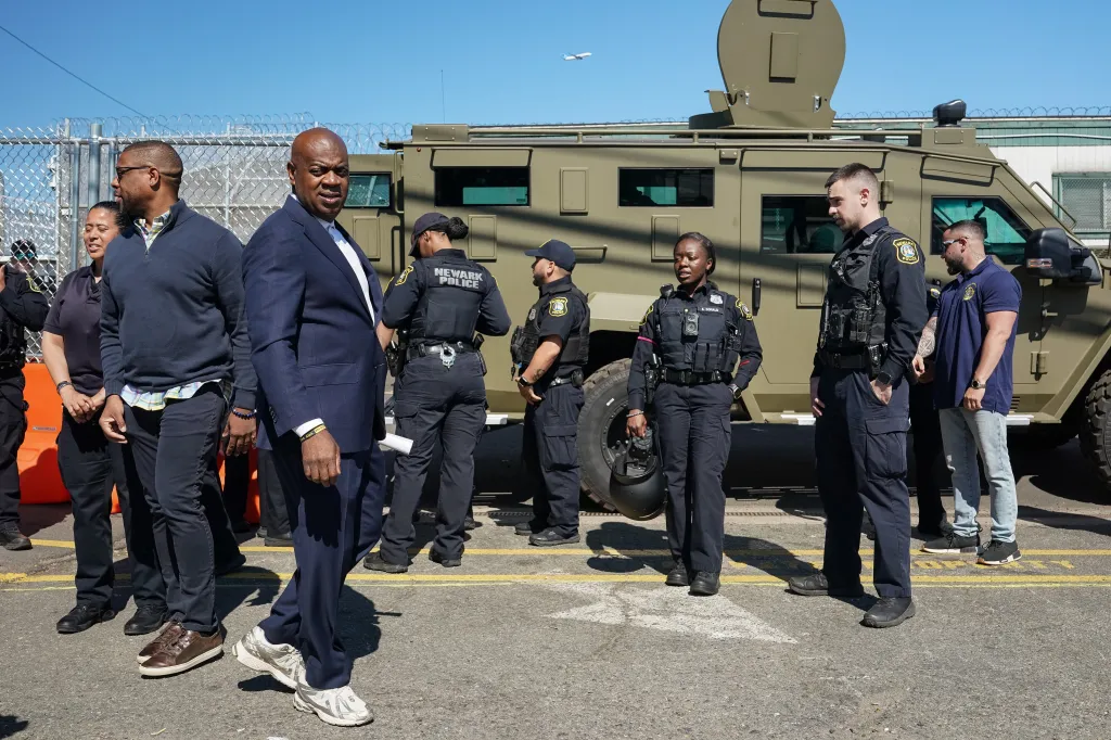 Newark Mayor Ras Baraka walking beside a green Lenco BearCat armored vehicle with Newark police officers.