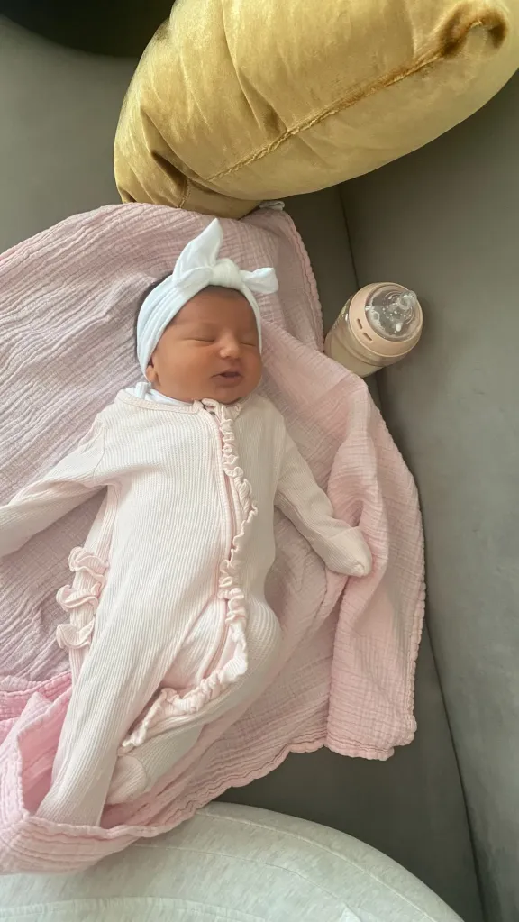 Newborn baby Ella sleeping on a pink blanket next to a baby bottle.