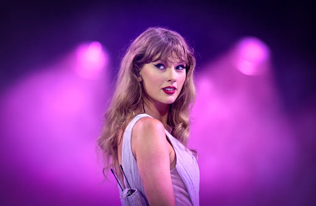 Taylor Swift performing on stage with a vibrant purple backdrop.