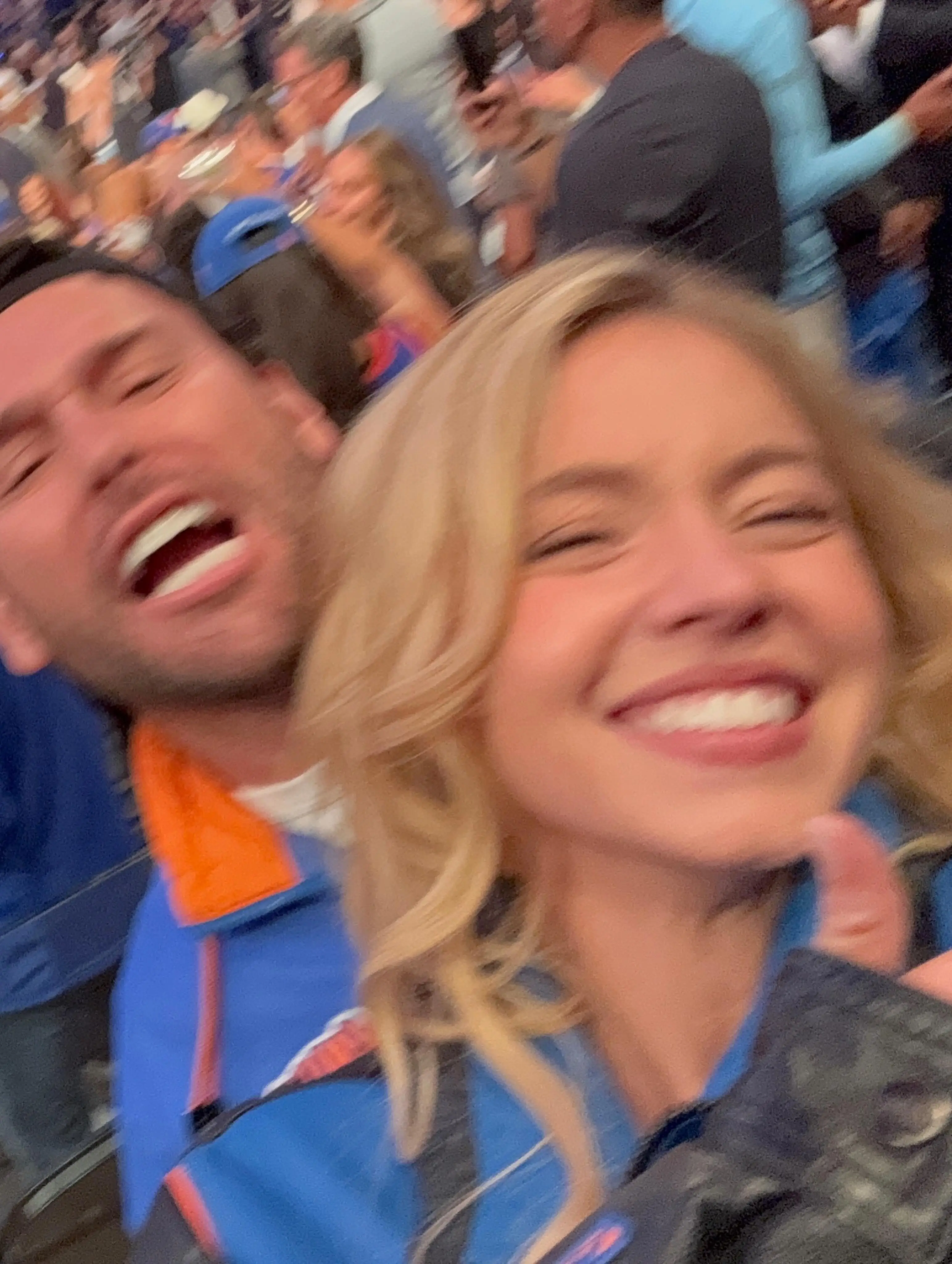 A man and woman smiling in the stands at a sporting event.