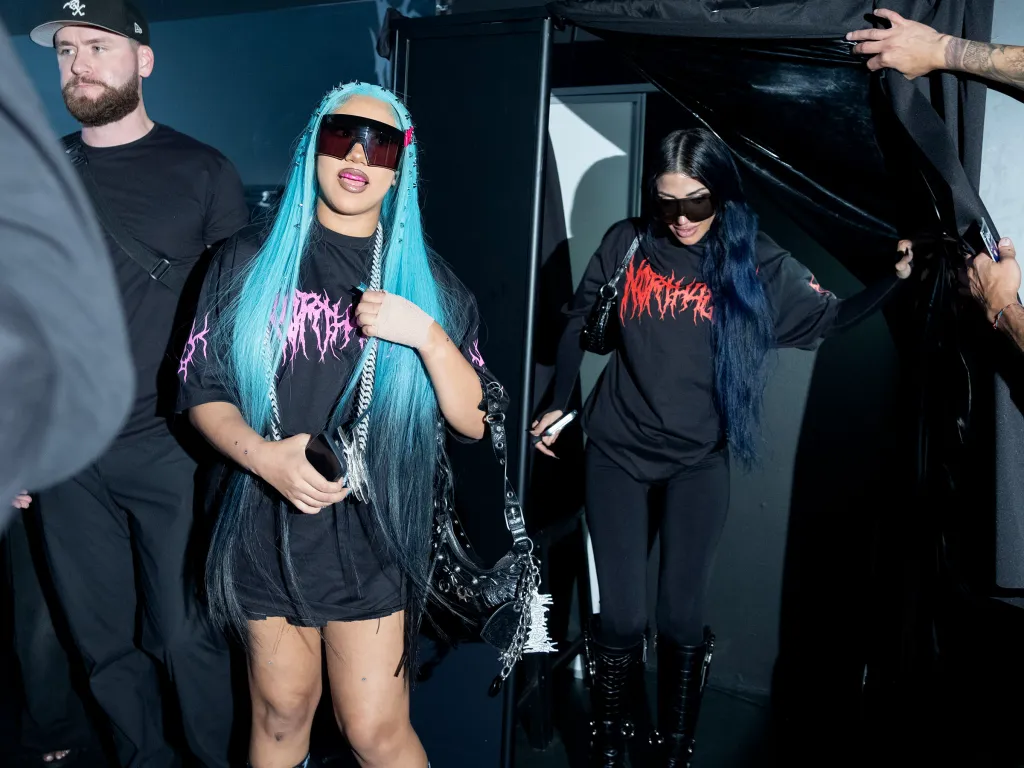 North West with blue hair and large sunglasses posing at a pop-up shop.