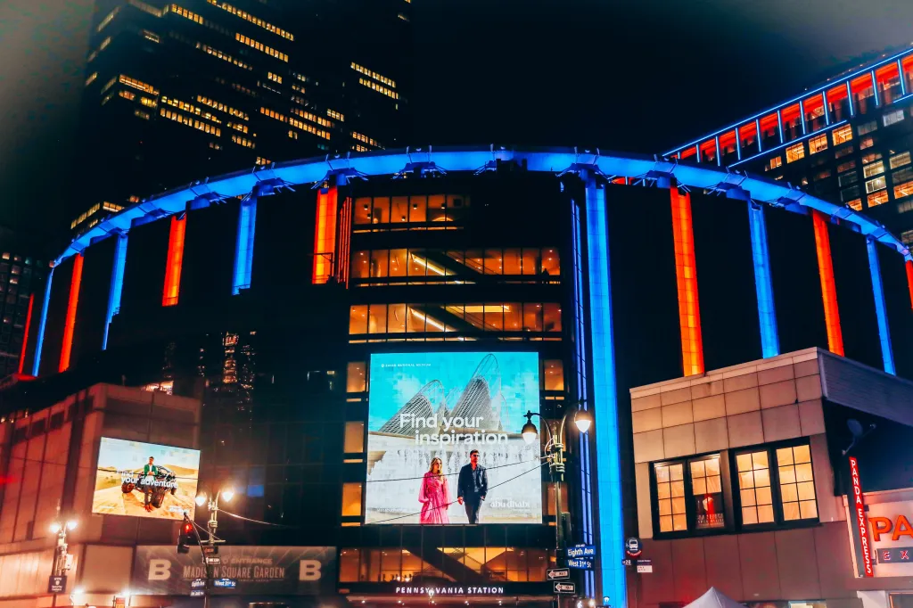 Madison Square Garden at night, lit in red and blue lights, with billboards advertising 