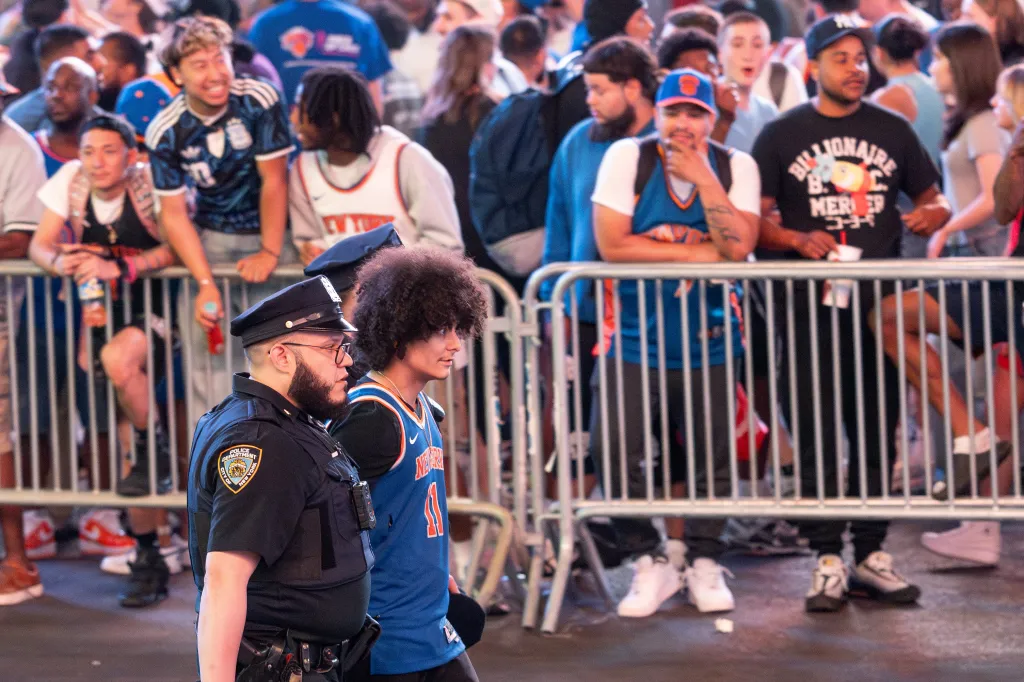 A NYPD officer and a fan in a New York Knicks jersey watch crowds outside Madison Square Garden during Game 2 of the NBA Finals.
