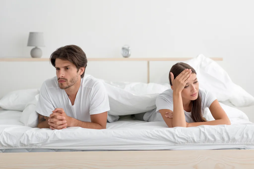 A man and woman lying on a bed with their backs to each other, indicating a quarrel or relationship crisis.