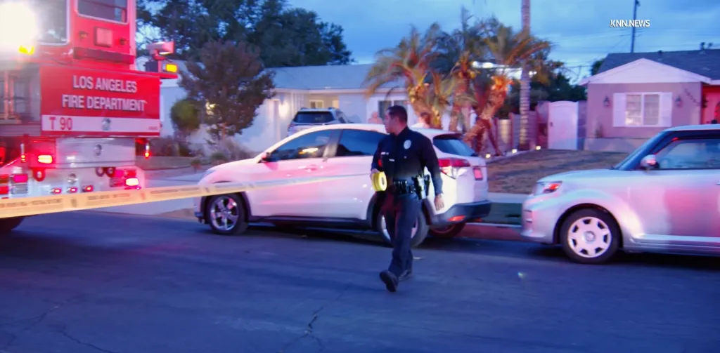 A police officer tapes off a crime scene with a fire truck and cars in the background.