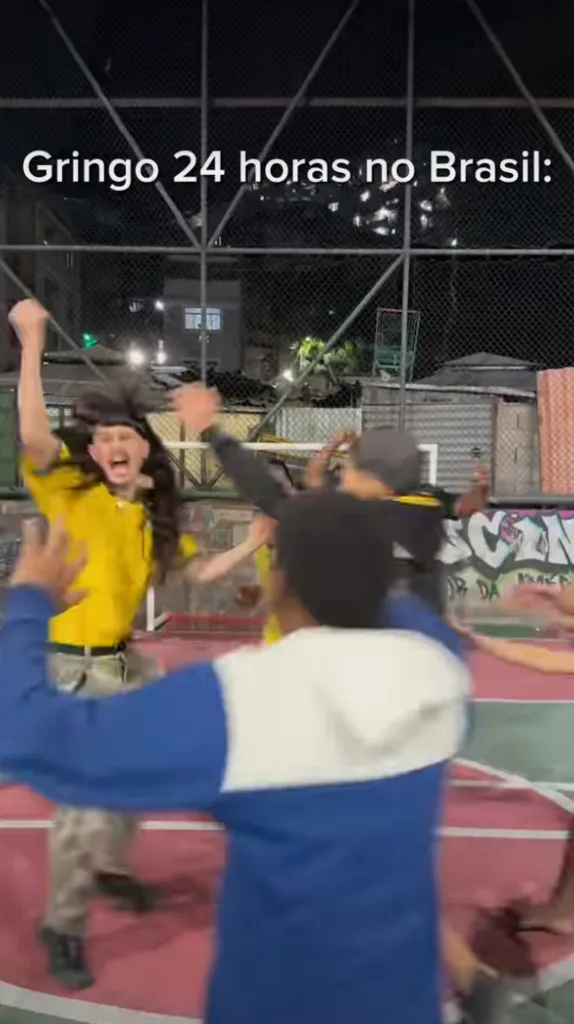 A group of people dancing outdoors at night with a person in a yellow shirt and long wig cheering.