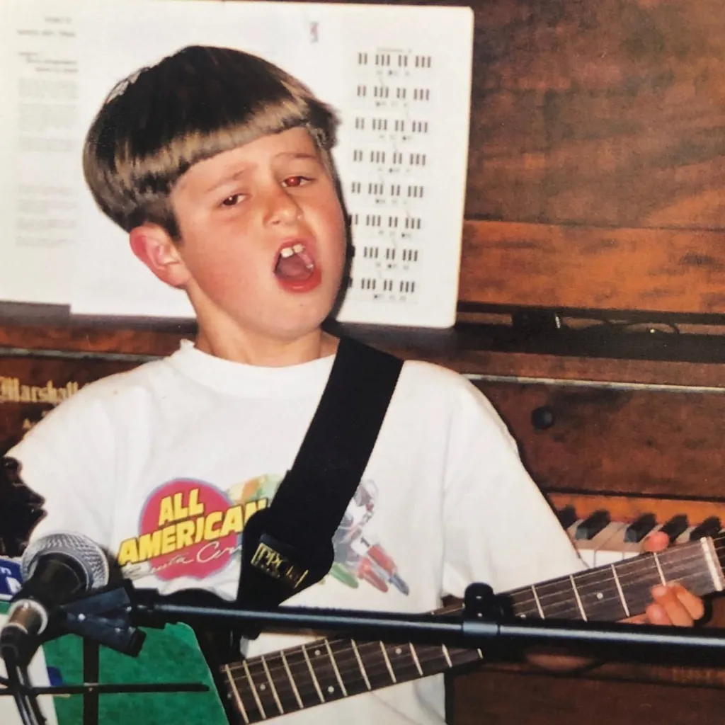 Young Oliver Tree playing guitar and singing into a microphone.